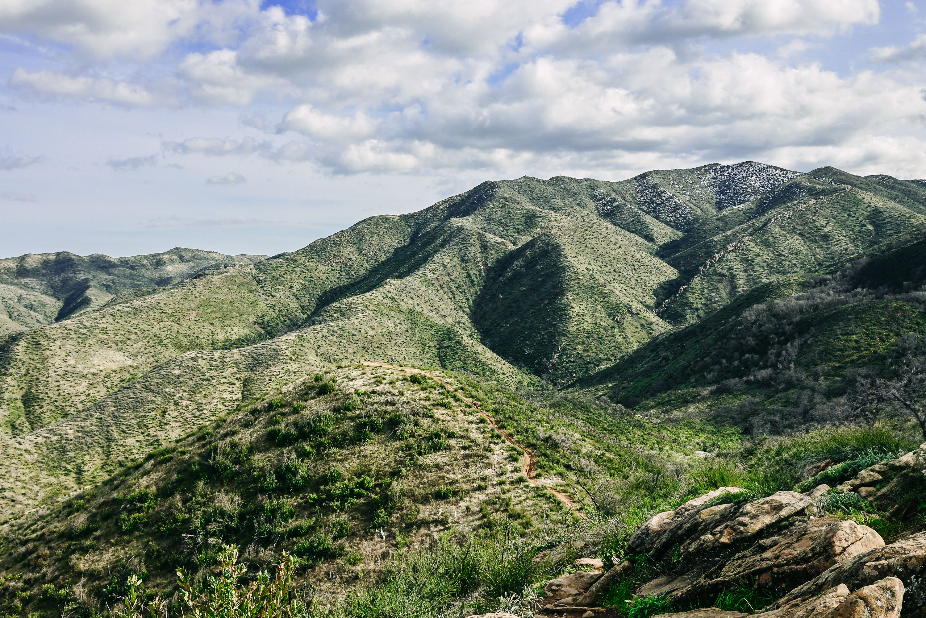Scenic path overlooking lush green valley mountains, set against a backdrop of stunning clouds and a vivid blue sky.